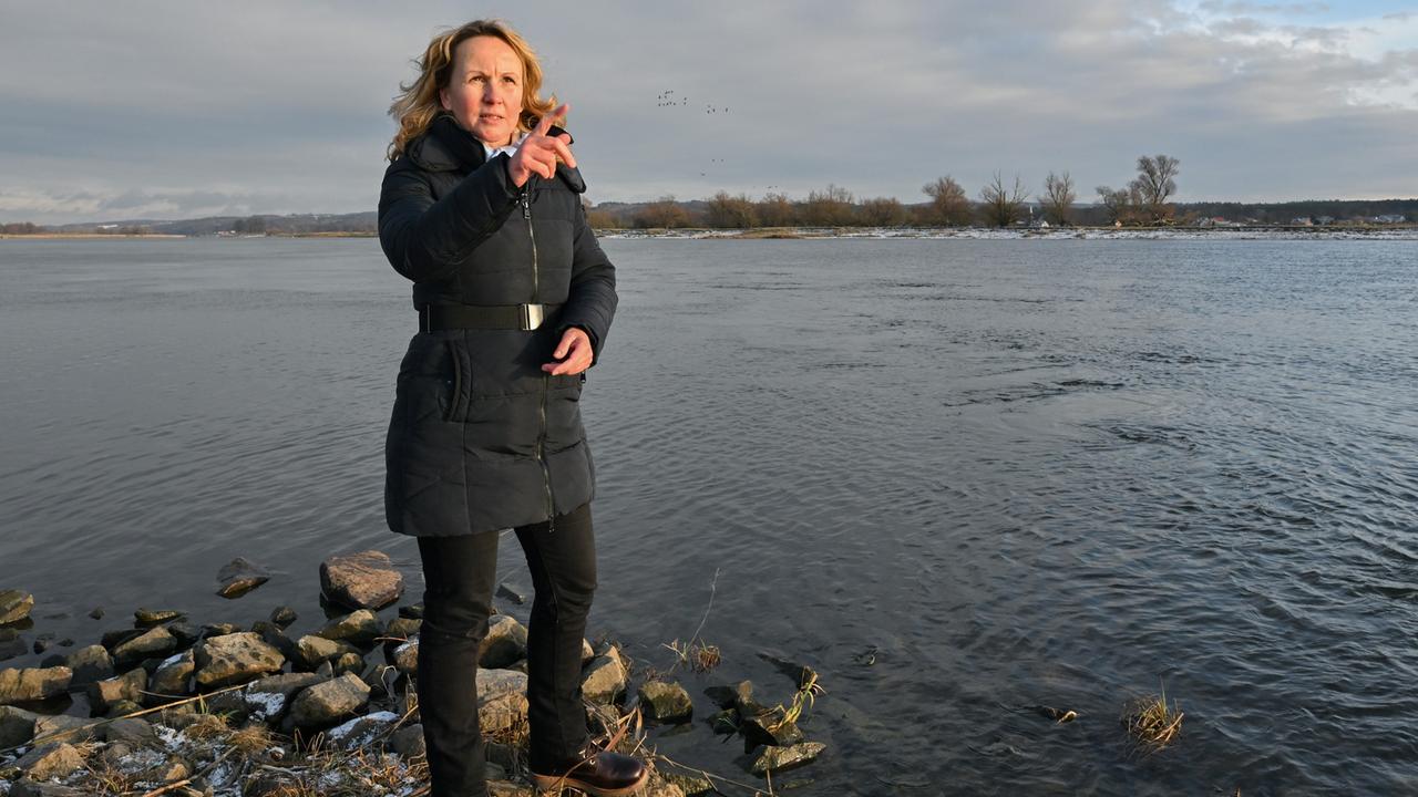 Steffi Lemke steht am Ufer eines Flusses. Sie trägt einen dunkelblauen Anorak und gestikuliert im Gespräch.