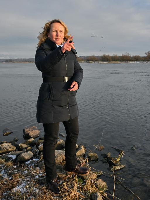 Steffi Lemke steht am Ufer eines Flusses. Sie trägt einen dunkelblauen Anorak und gestikuliert im Gespräch.