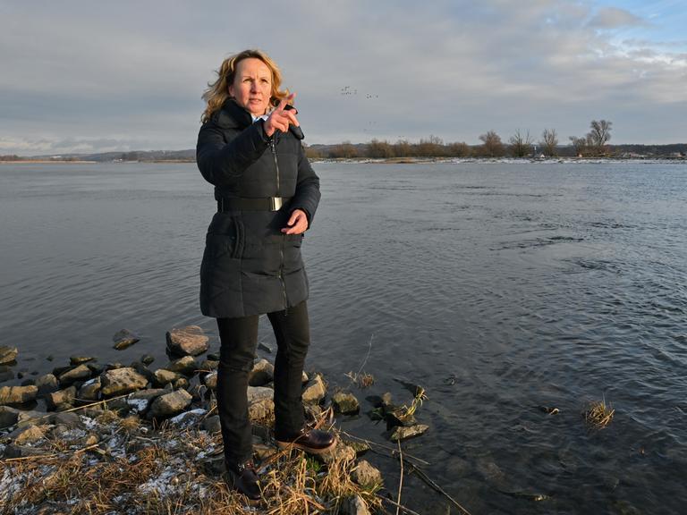 Steffi Lemke steht am Ufer eines Flusses. Sie trägt einen dunkelblauen Anorak und gestikuliert im Gespräch.