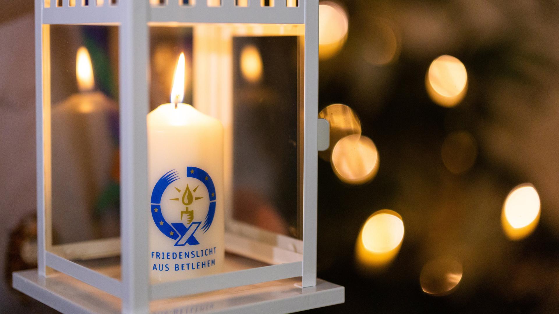 Eine Kerze mit der Aufschrift "Friedenslicht aus Bethlehem" brennt in einem Windlichtgehäuse.