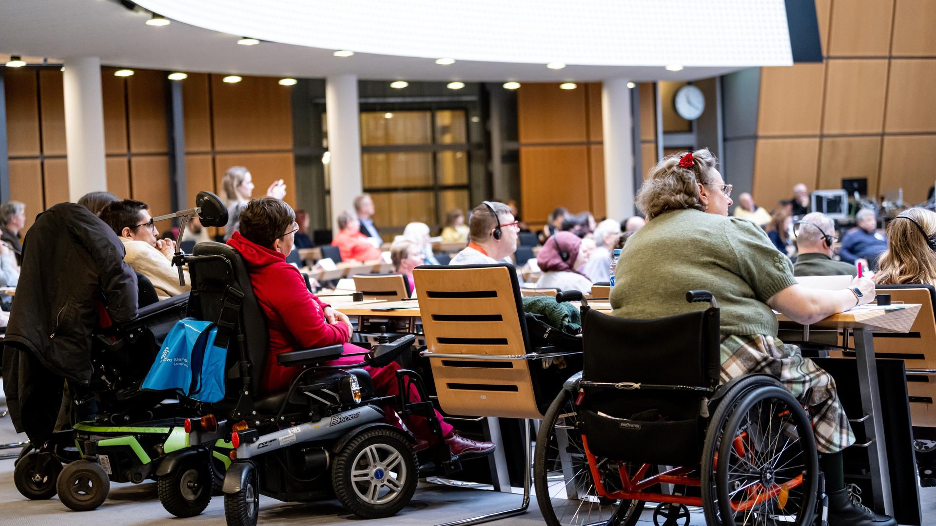 Mehrere Menschen sitzen in Roll-Stühlen an einem Konferenz-Tisch. Es sind Mitglieder von dem Behinderten-Parlament in Berlin.