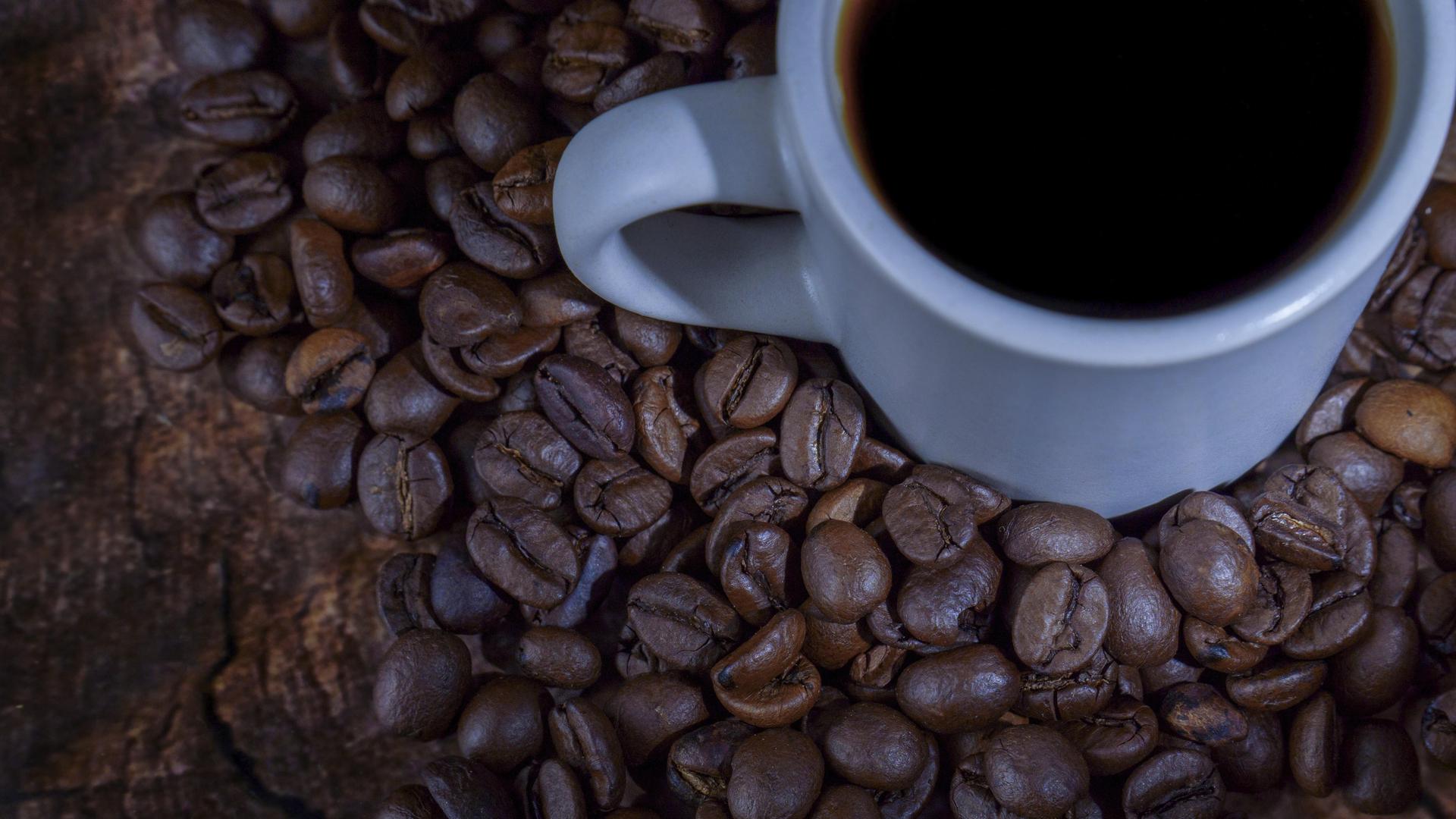 Weiße Keramiktasse mit dunklem Kaffee, die auf einem Bett aus Kaffeebohnen und einer rustikalen Holzoberfläche ruht
