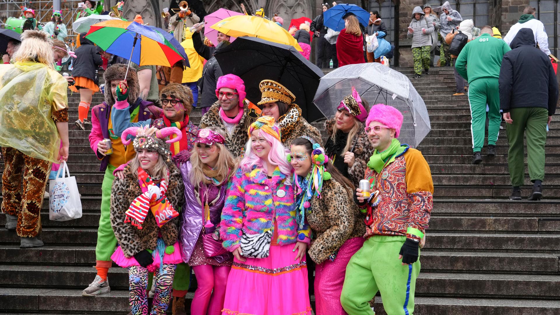 Verkleidete Menschen stehen auf einer Treppe in Köln, sie halten Regen-Schirme.