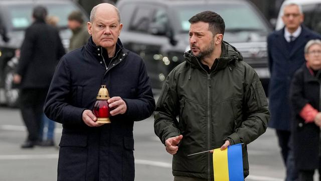 Bundeskanzler Scholz und der ukrainische Präsident Selenskyj gehen zu einem Mahnmal für gefallene Soldaten. Scholz hat eine Laterne, Selenskyj eine ukrainische Fahne in der Hand.