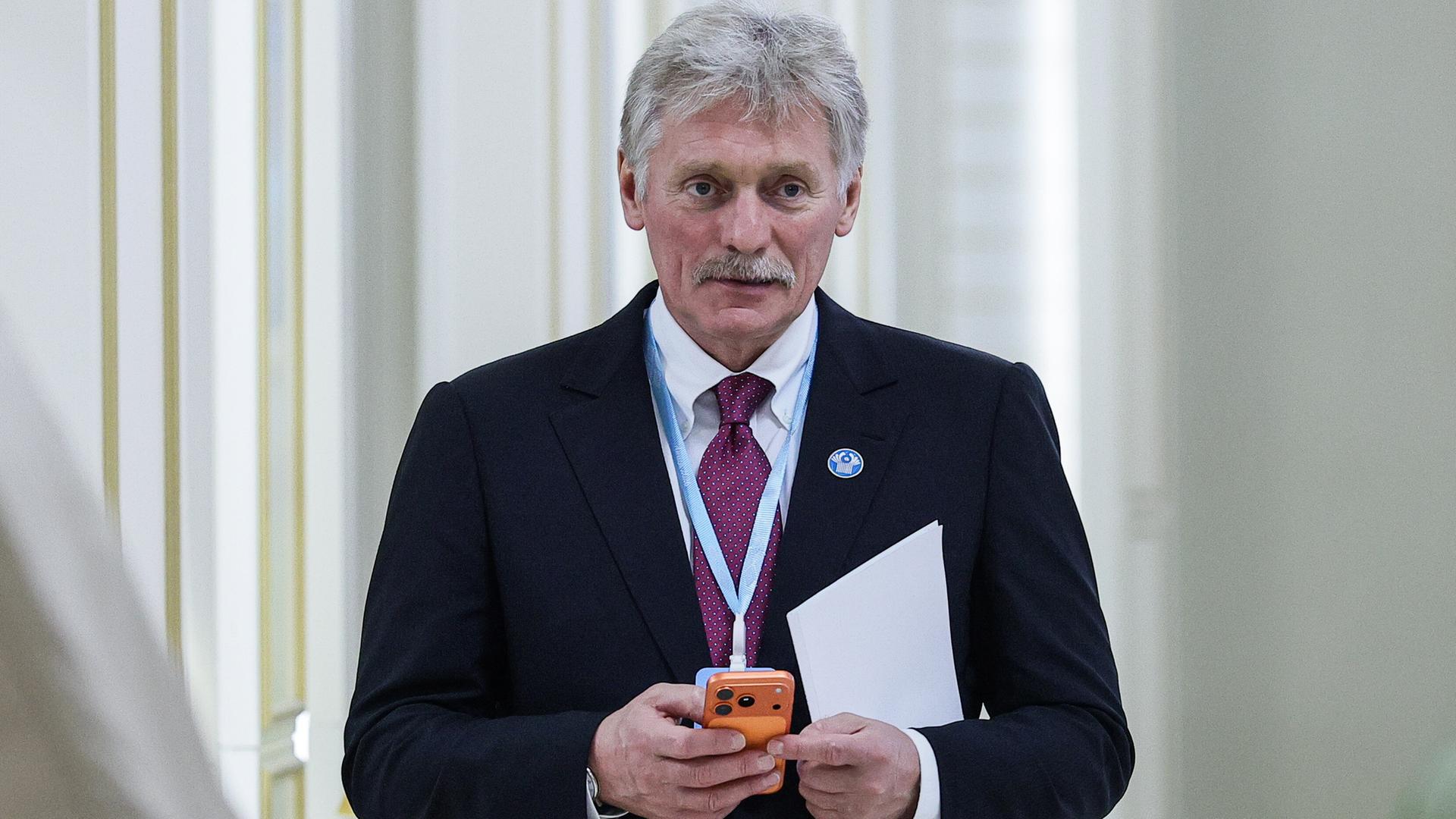 Kreml-Sprecher Dimitri Peskow hält ein Smartphone in der Hand. 