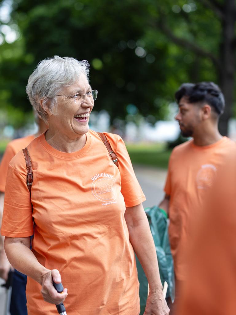 Eine Gruppe von Frauen und Männern in organgefarbenen Tshirts steht in fröhlich in einem Park, den sie gerade reinigen