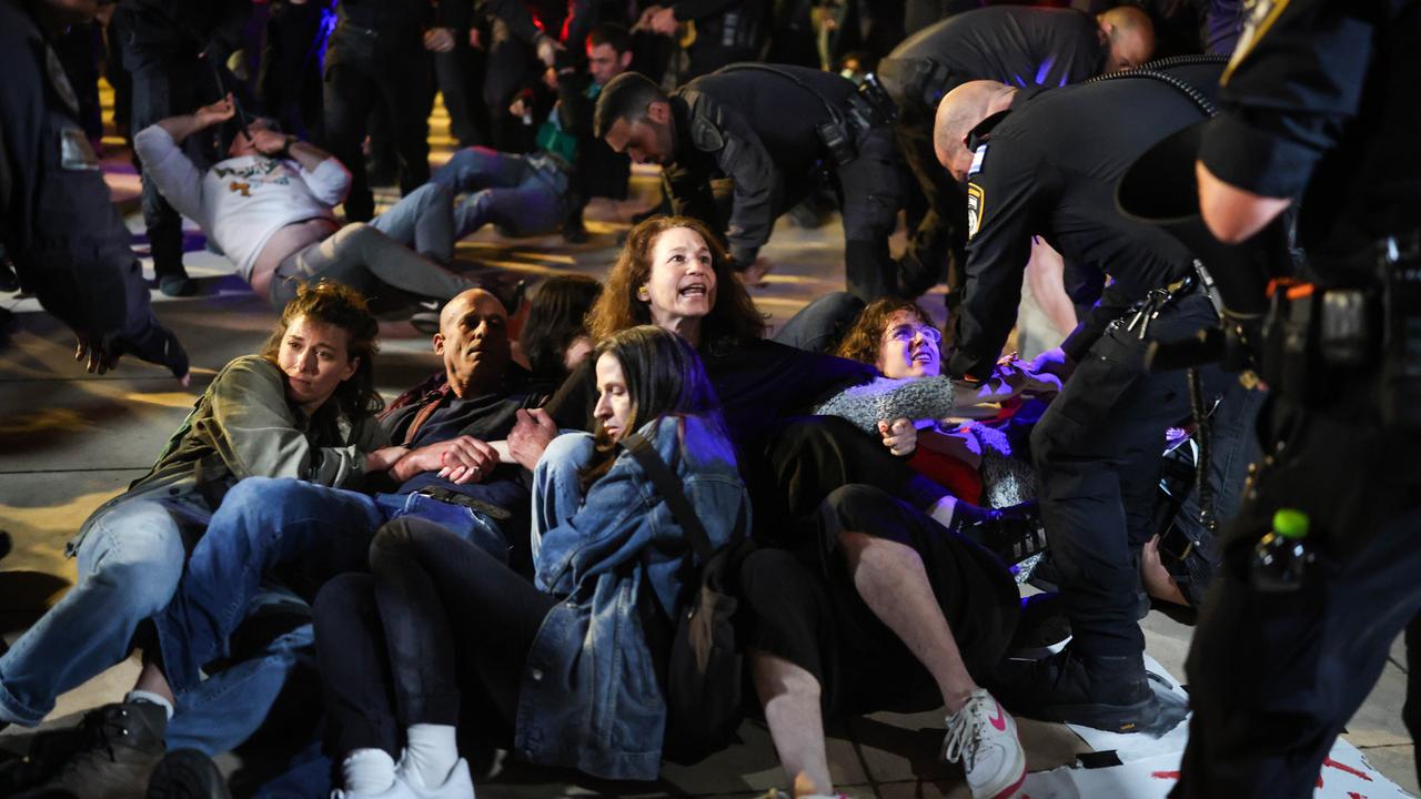 Mehrere Demonstranten sitzen in der israelischen Stadt Tel Aviv am Boden und halten sich aneinander fest. Polizisten versuchen, die Demonstranten wegzuziehen.