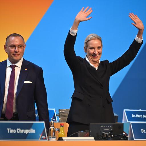 Weidel und Chrupalla stehen nebeneinander auf der Parteitagsbühne. Weidel winkt mit beiden Händen.