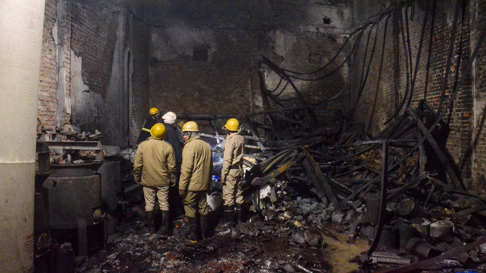 Feuerwehrleute schauen zu, nachdem sie am späten Donnerstag ein Feuer in einer Farbenfabrik im Stadtteil Alipur im Norden von Neu-Delhi, Indien, gelöscht haben. Feuerwehrleute schauen zu, nachdem sie am späten Donnerstag ein Feuer in einer Farbenfabrik im Stadtteil Alipur im Norden von Neu-Delhi, Indien, gelöscht haben.