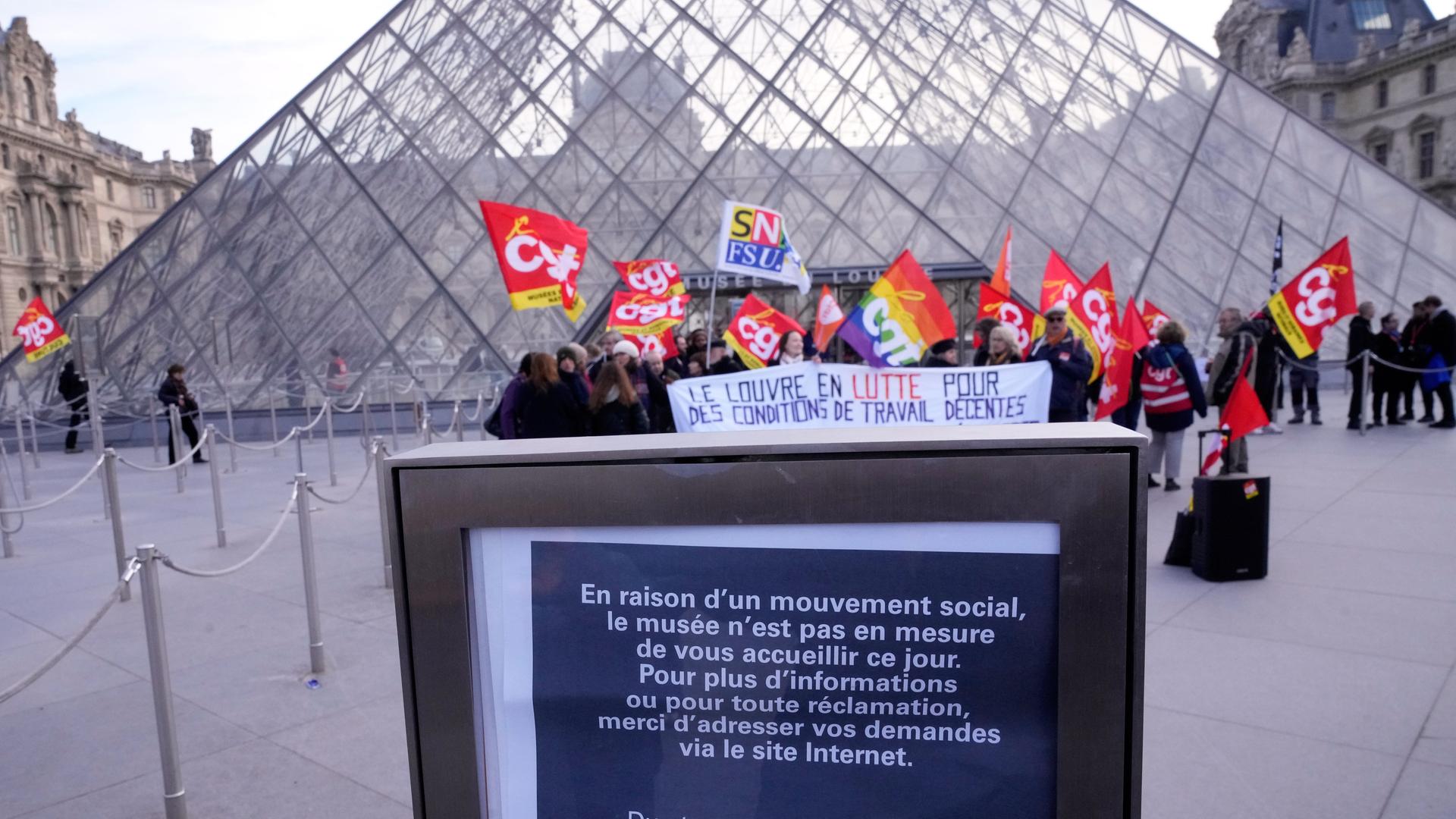 Streikende Mitarbeiter des Museums stehen mit Fahnen vor der Glaskuppel des Museums. Vor ihnen ein Hinweisschild, dass das Museum geschlossen bleibt. Streikende Mitarbeiter des Museums stehen mit Fahnen vor der Glaskuppel des Museums. Vor ihnen ein Hinweisschild, dass das Museum geschlossen bleibt.