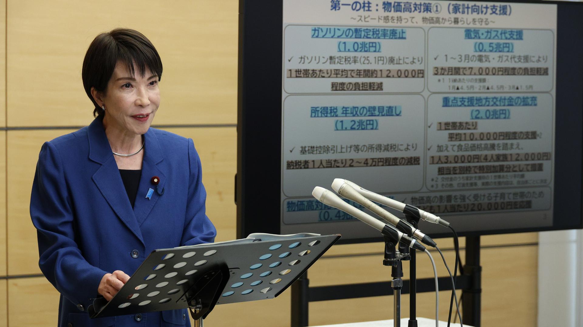 Japans Ministerpräsidentin Takaichi steht an einem Rednerpult, hinter ihr ein Bildschirm mit japanischem Text.