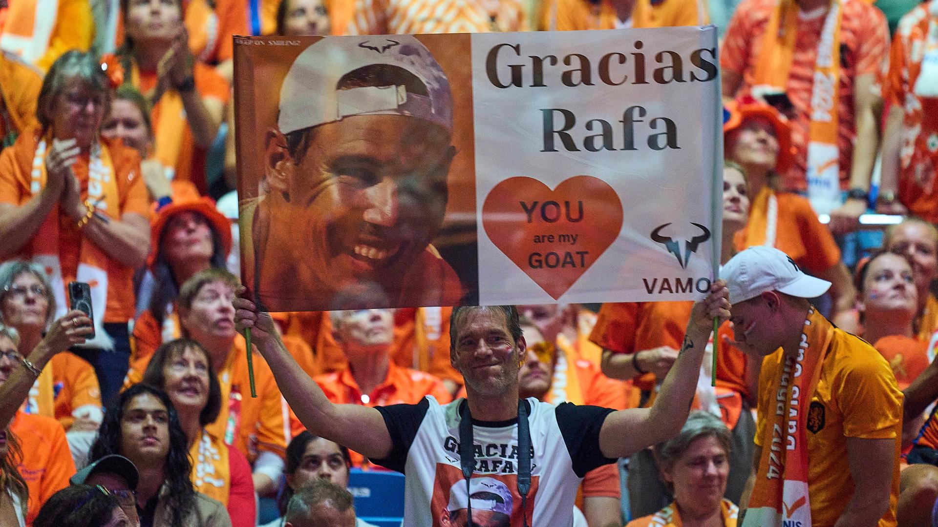 Zu sehen sind Fans, die ein Banner hochhalten, auf dem ein Foto von Rafael Nadal gedruckt ist und "Gracias Rafa" steht.