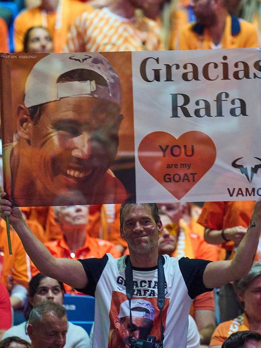 Zu sehen sind Fans, die ein Banner hochhalten, auf dem ein Foto von Rafael Nadal gedruckt ist und "Gracias Rafa" steht.