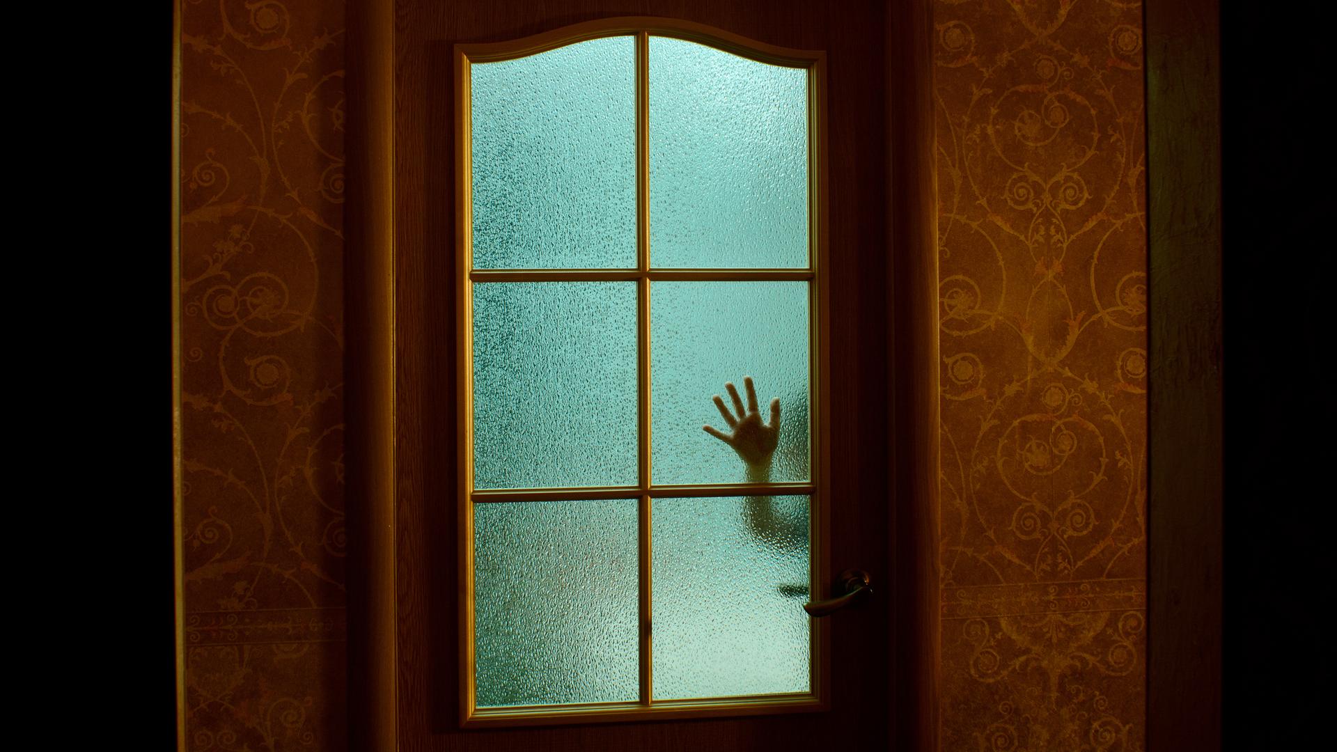 Eine Kinderhand an einer geschlossenen Glastür, in gruseliger Atmosphäre.