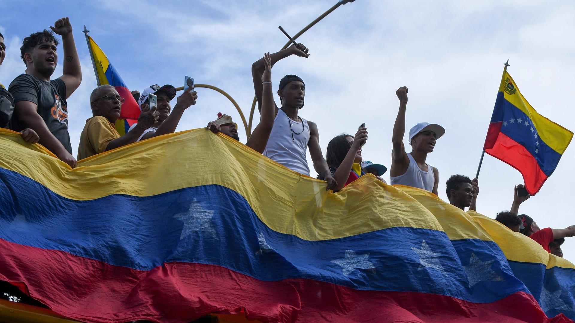 Demonstranten halten eine Landesfahne Venezuelas vor sich, andere halten eine Flagge.