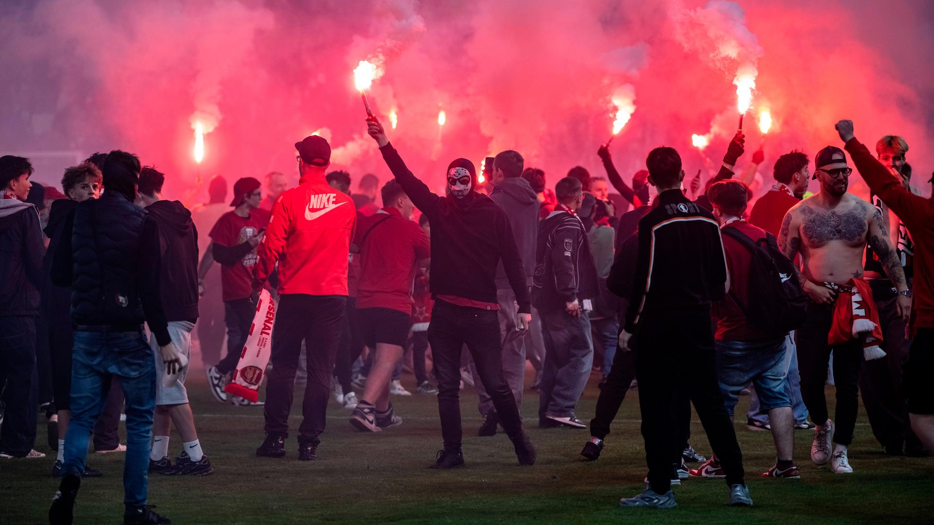Auf dem Spielfeld stehen zum Teil vermummte Fans und zünden Pyrotechnik. Die Luft ist rot durch den Rauch der Bengalos. Auf dem Spielfeld stehen zum Teil vermummte Fans und zünden Pyrotechnik. Die Luft ist rot durch den Rauch der Bengalos.