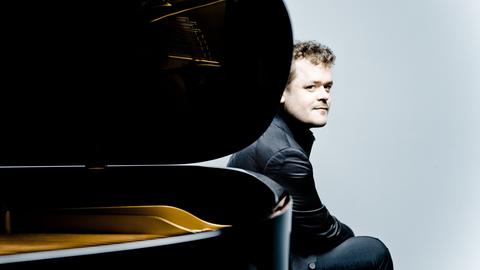 Der Pianist Benjamin Grosvenor sitzt am hinteren Ende eines aufgeklappten Flügels und schaut an der Rundung des Instrumentes vorbei.