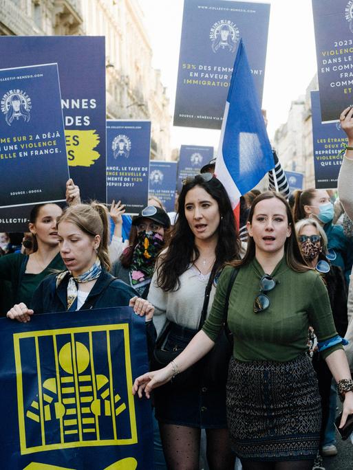 Eine Gruppe von demonstrierenden Frauen läuft durch die Straßen von Paris. Sie halten Schilder in die Luft. 