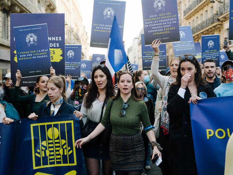 Eine Gruppe von demonstrierenden Frauen läuft durch die Straßen von Paris. Sie halten Schilder in die Luft. 