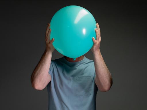 Porträt eines Mannes, der einen hellblauen Luftballon vor sein Gesicht hält.