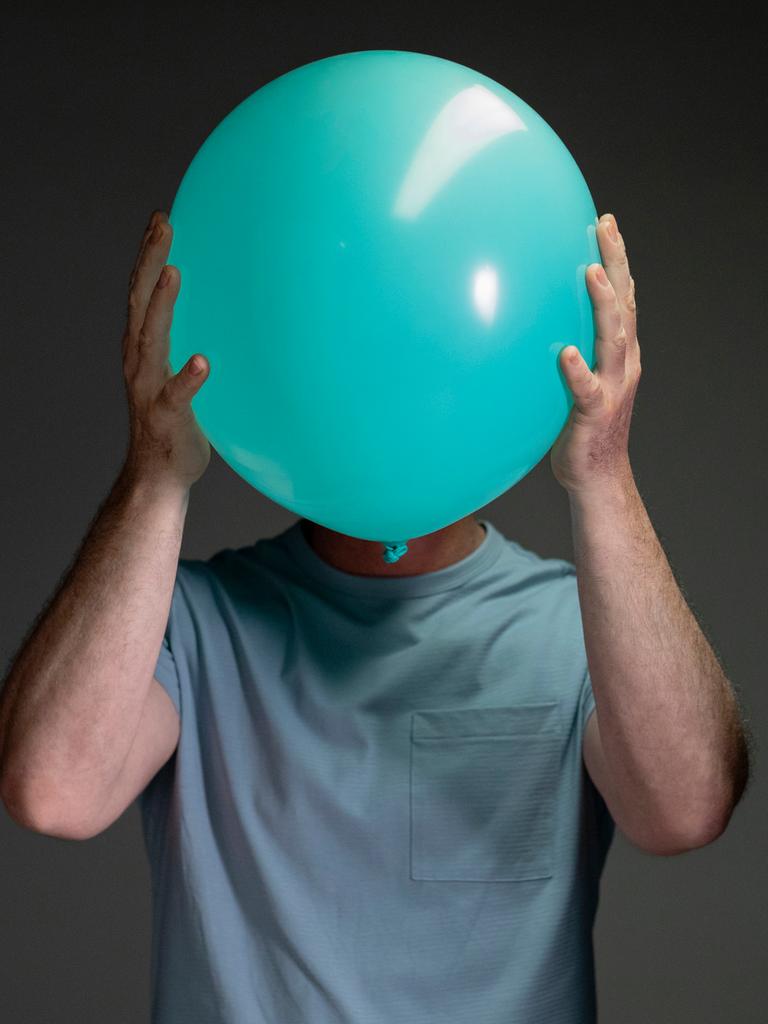 Porträt eines Mannes, der einen hellblauen Luftballon vor sein Gesicht hält.