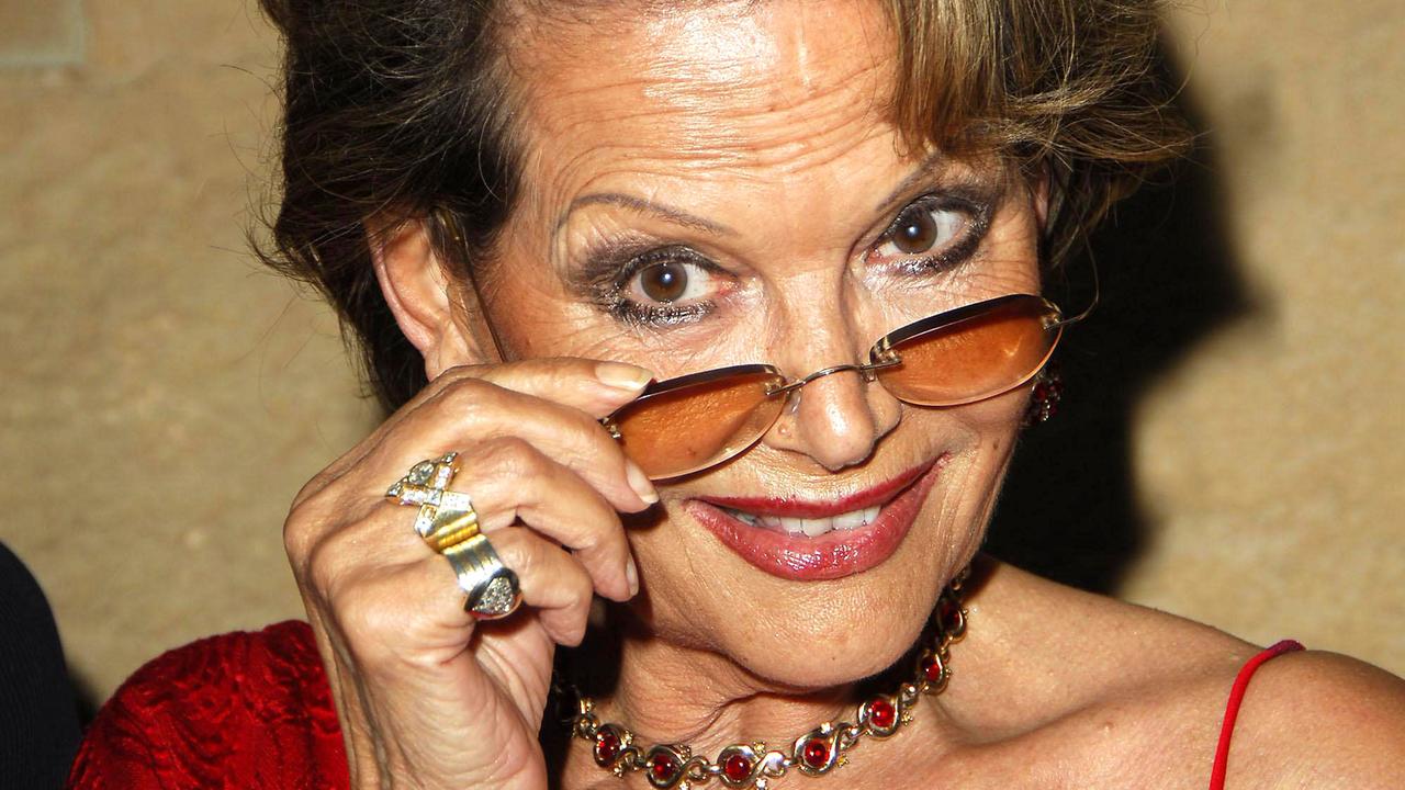 Claudia Cardinale posiert für die Kamera. Sie zieht ihre Brille auf die Nasenspitze und blickt darüber.