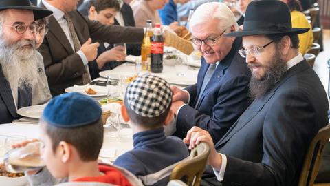 Frank-Walter Steinmeier sitzt mit orthodox gekleideten Juden an einem Tisch beim Essen und spricht mit aus der Ukraine geflüchteten Kindern.