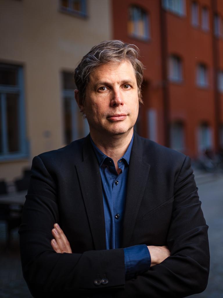 Daniel Kehlmann steht mit verschränkten Armen in einem Innenhof und blickt ernst in die Kamera.