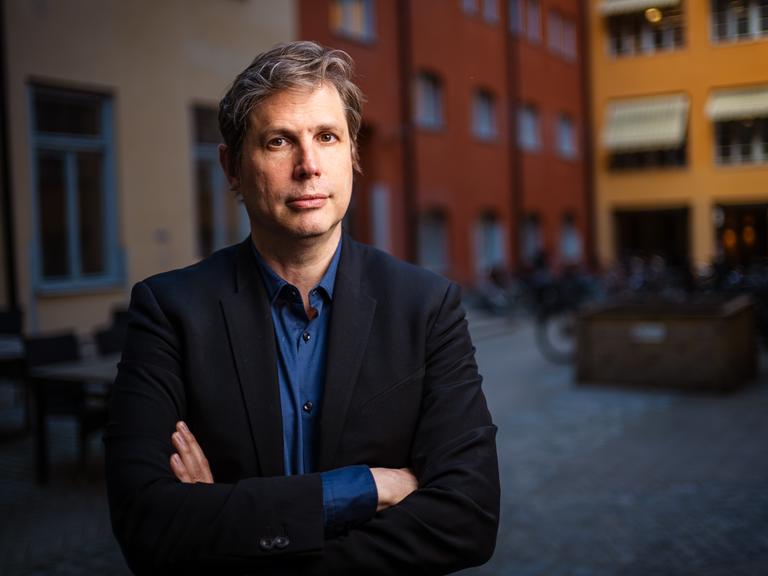 Daniel Kehlmann steht mit verschränkten Armen in einem Innenhof und blickt ernst in die Kamera. Daniel Kehlmann steht mit verschränkten Armen in einem Innenhof und blickt ernst in die Kamera.