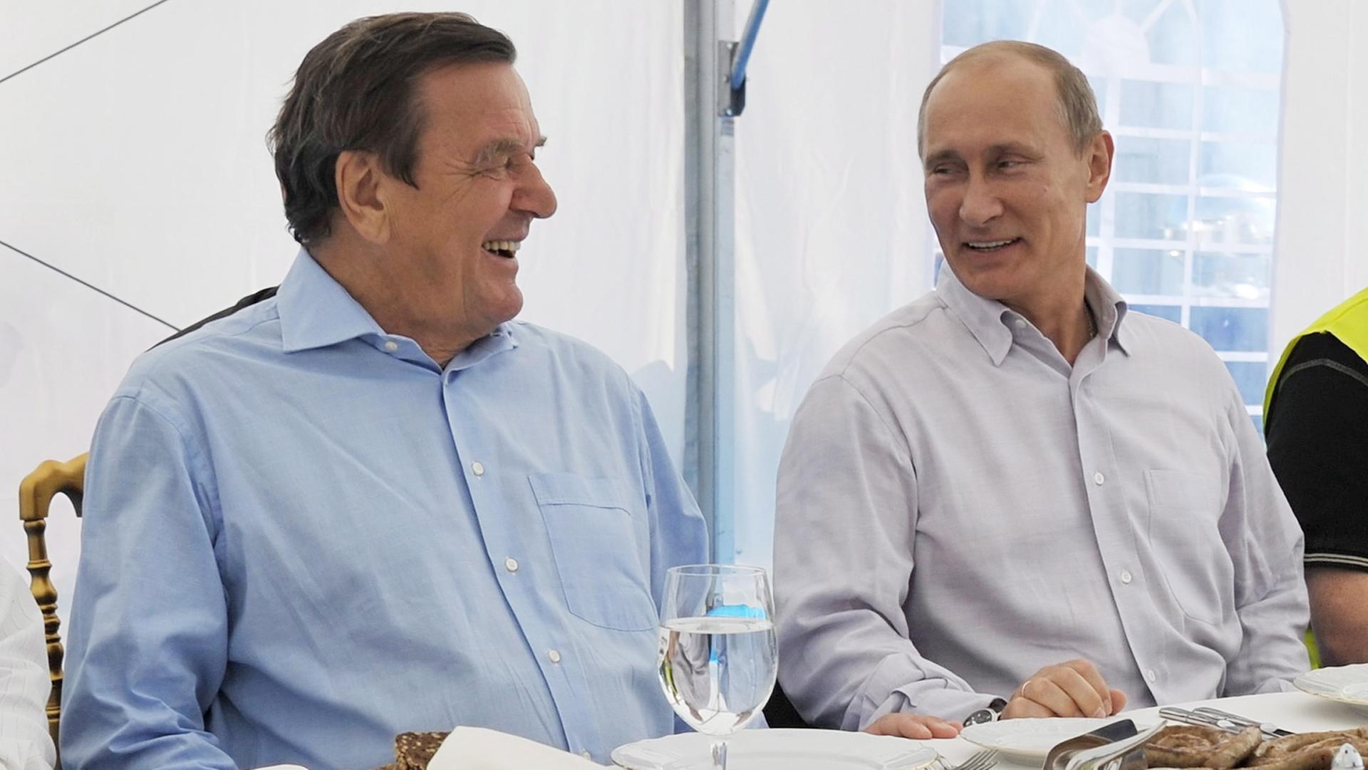Russlands Präsident Wladimir Putin und der frühere Bundeskanzler Gerhard Schröder gemeinsam an einem gedeckten Tisch 2011 bei einem Treffen in Russland.