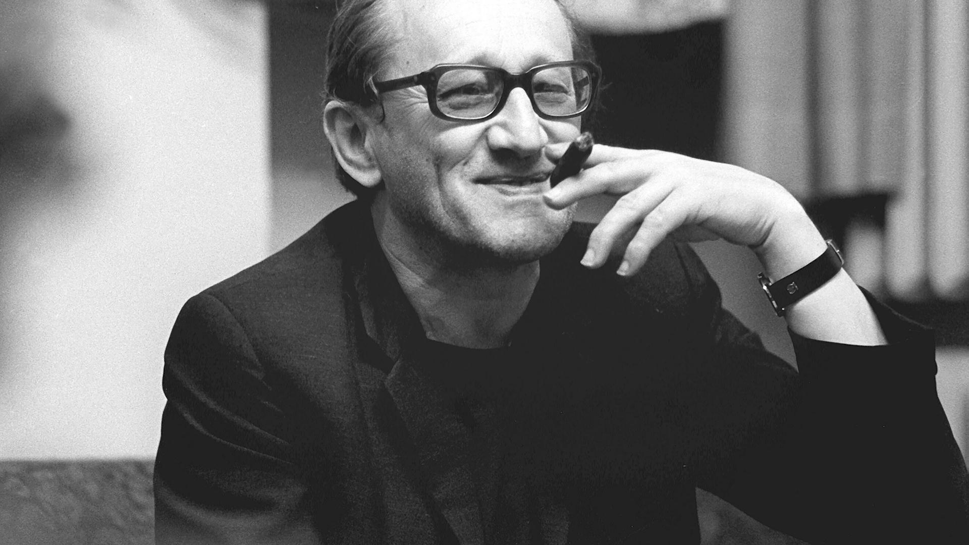 Der deutsche Dramatiker und Lyriker Heiner Müller lächelt und hält eine Zigarre in einer Schwarzweiß-Aufnahme von 1987