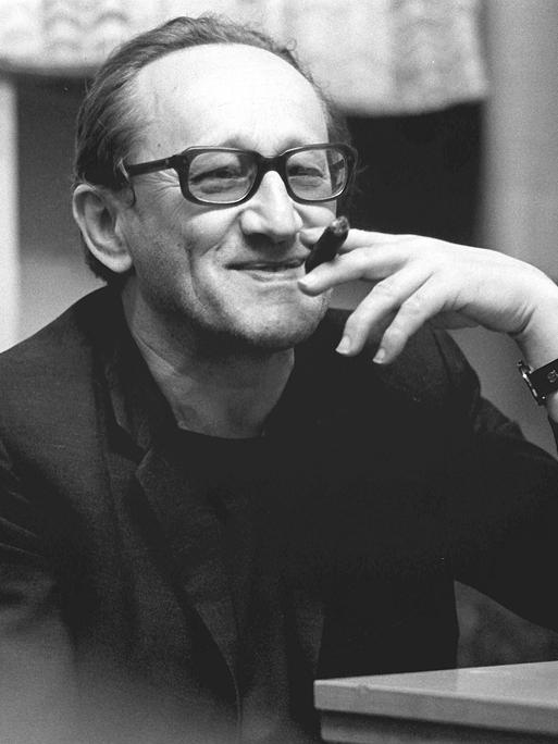 Der deutsche Dramatiker und Lyriker Heiner Müller lächelt und hält eine Zigarre in einer Schwarzweiß-Aufnahme von 1987