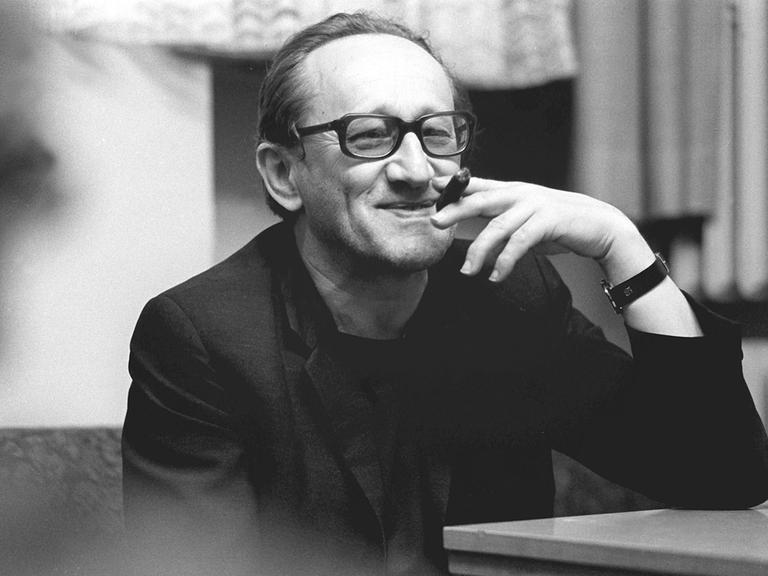 Der deutsche Dramatiker und Lyriker Heiner Müller lächelt und hält eine Zigarre in einer Schwarzweiß-Aufnahme von 1987