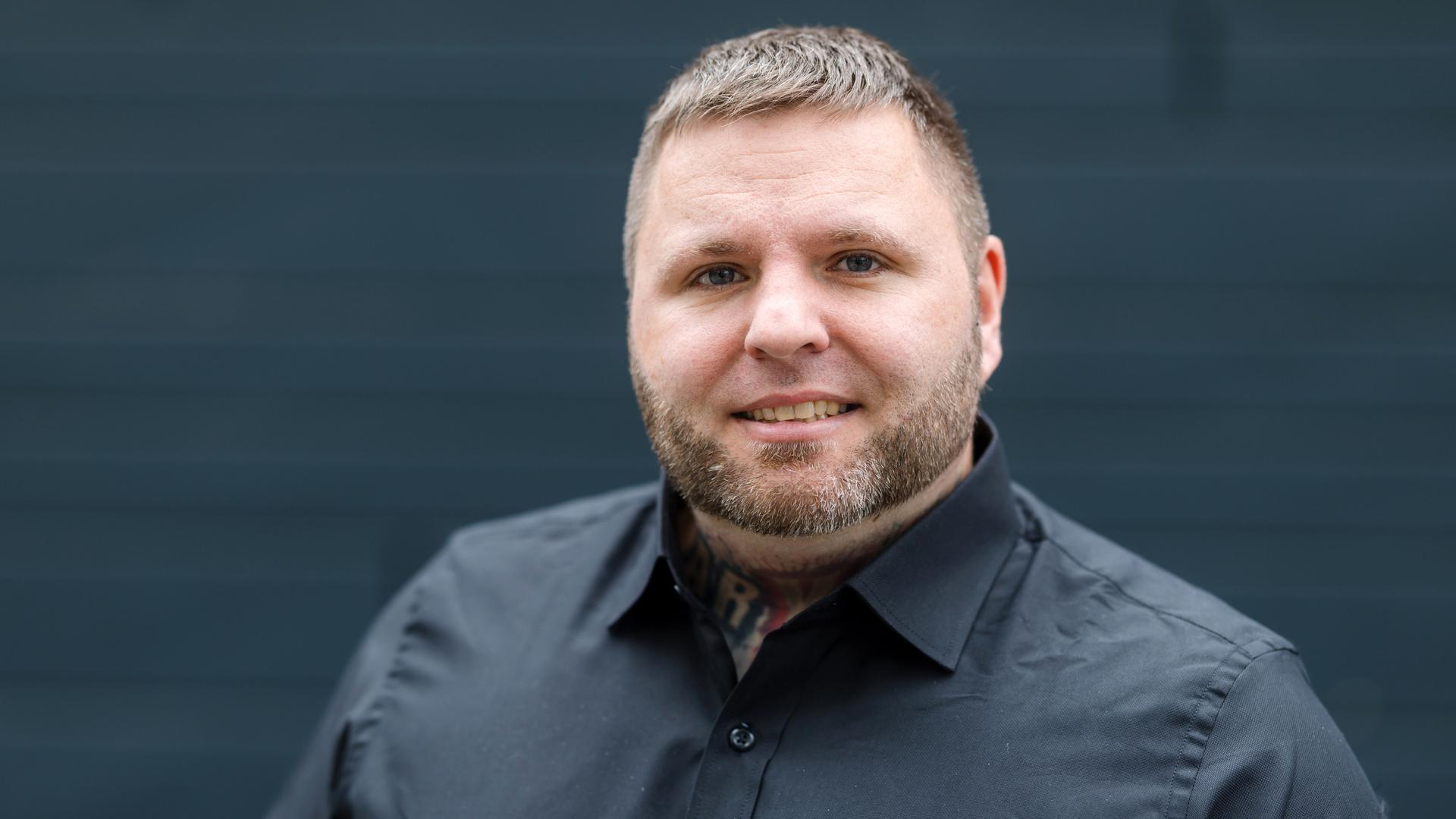 Tommy Frenck steht in schwarzem Hemd vor schwarzem Hintergrund und guckt in die Kamera. Tommy Frenck steht in schwarzem Hemd vor schwarzem Hintergrund und guckt in die Kamera.