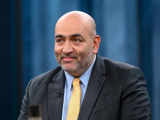 Porträt von Omid Nouripour (51 Jahre alter Mann mit kräftiger Statur, Glatze, gelber Krawatte und schwarzem Sacko), Vizepräsident des Deutschen Bundestages, Bündnis 90/Die Grünen als Gast beim Politiktalk Caren Miosga