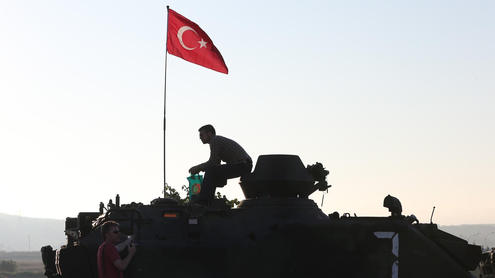 Die Silhouette eines Mannes auf einem gepanzerten Fahrzeug zeichnet sich gegen den Morgenhimmel ab. Auf dem Fahrzeug ist die türkische Nationalflagge gehisst.