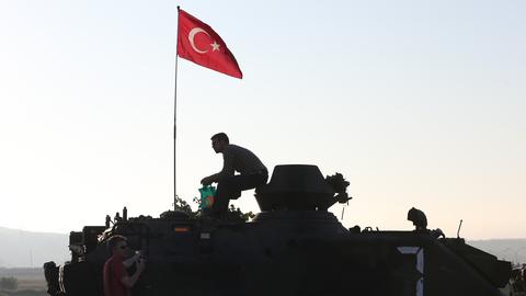 Die Silhouette eines Mannes auf einem gepanzerten Fahrzeug zeichnet sich gegen den Morgenhimmel ab. Auf dem Fahrzeug ist die türkische Nationalflagge gehisst.