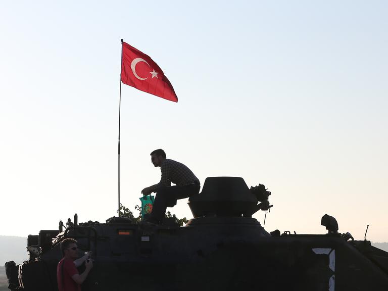 Die Silhouette eines Mannes auf einem gepanzerten Fahrzeug zeichnet sich gegen den Morgenhimmel ab. Auf dem Fahrzeug ist die türkische Nationalflagge gehisst. Die Silhouette eines Mannes auf einem gepanzerten Fahrzeug zeichnet sich gegen den Morgenhimmel ab. Auf dem Fahrzeug ist die türkische Nationalflagge gehisst.
