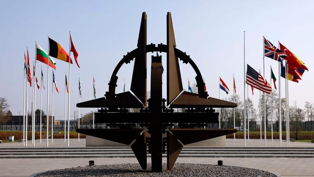 Blick auf die NATO-Sternenskulptur am Sitz der NATO in Brüssel, im Hintergrund wehen die Flaggen der Mitgliedstaaten an Fahnenmasten.
