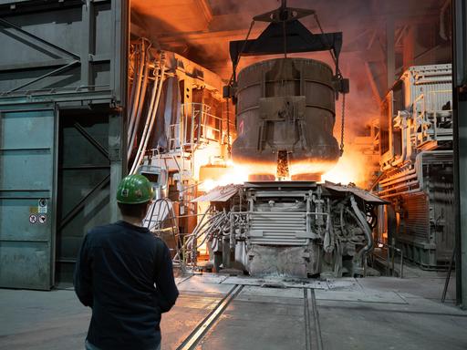Ein Mitarbeiter steht in einer Werkhalle der BGH Edelstahl Freital GmbH hinter einem Schrottkorb an einem Lichtbogenofen. Ein Mitarbeiter steht in einer Werkhalle der BGH Edelstahl Freital GmbH hinter einem Schrottkorb an einem Lichtbogenofen.