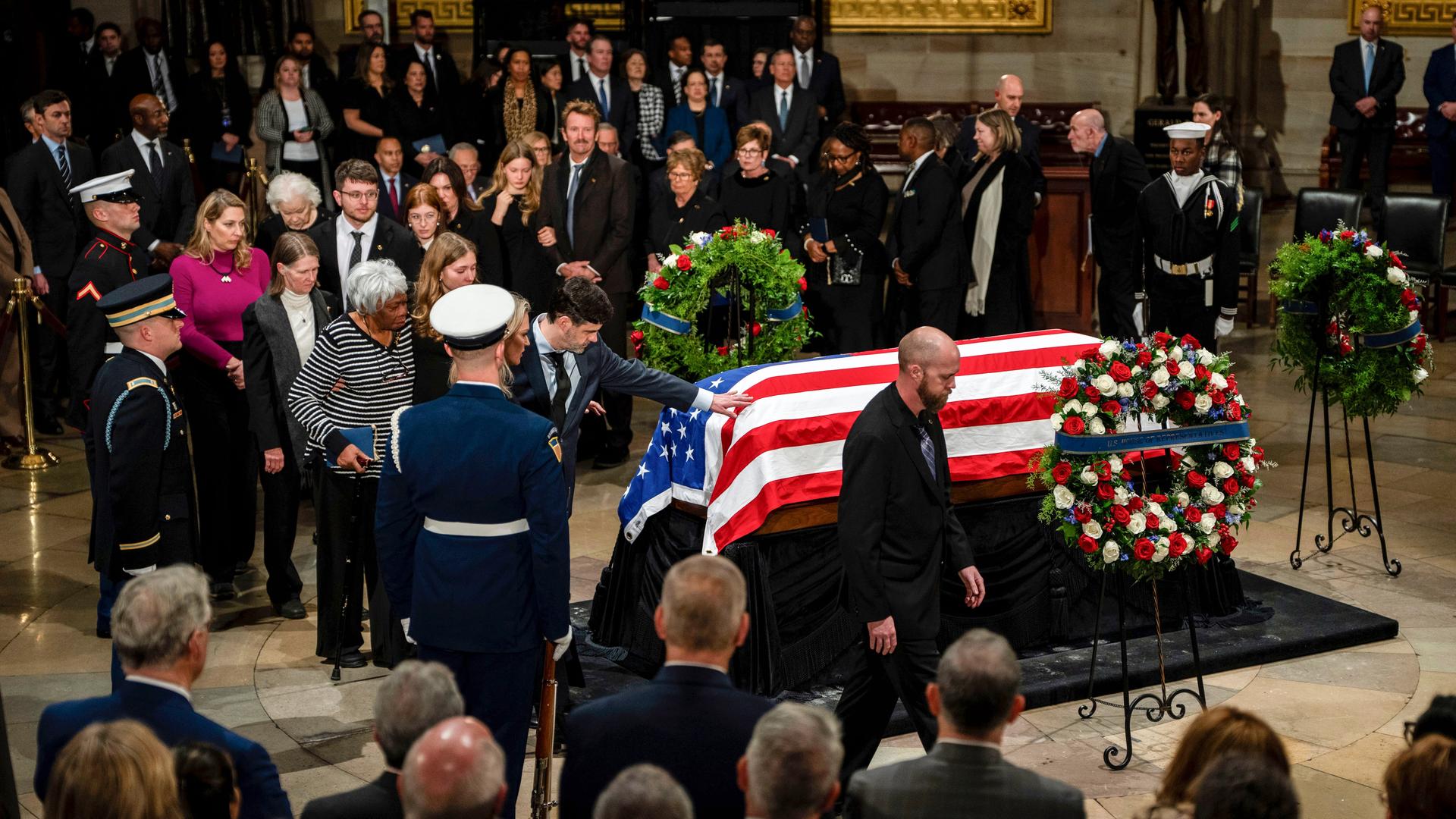 Der mit einer amerikanischen Flagge bedeckten Sarg Jimmy Carters ist im Kapitol aufgebahrt. Um ihn herum sind Menschen zu sehen, die sich von ihm verabschieden wollen.