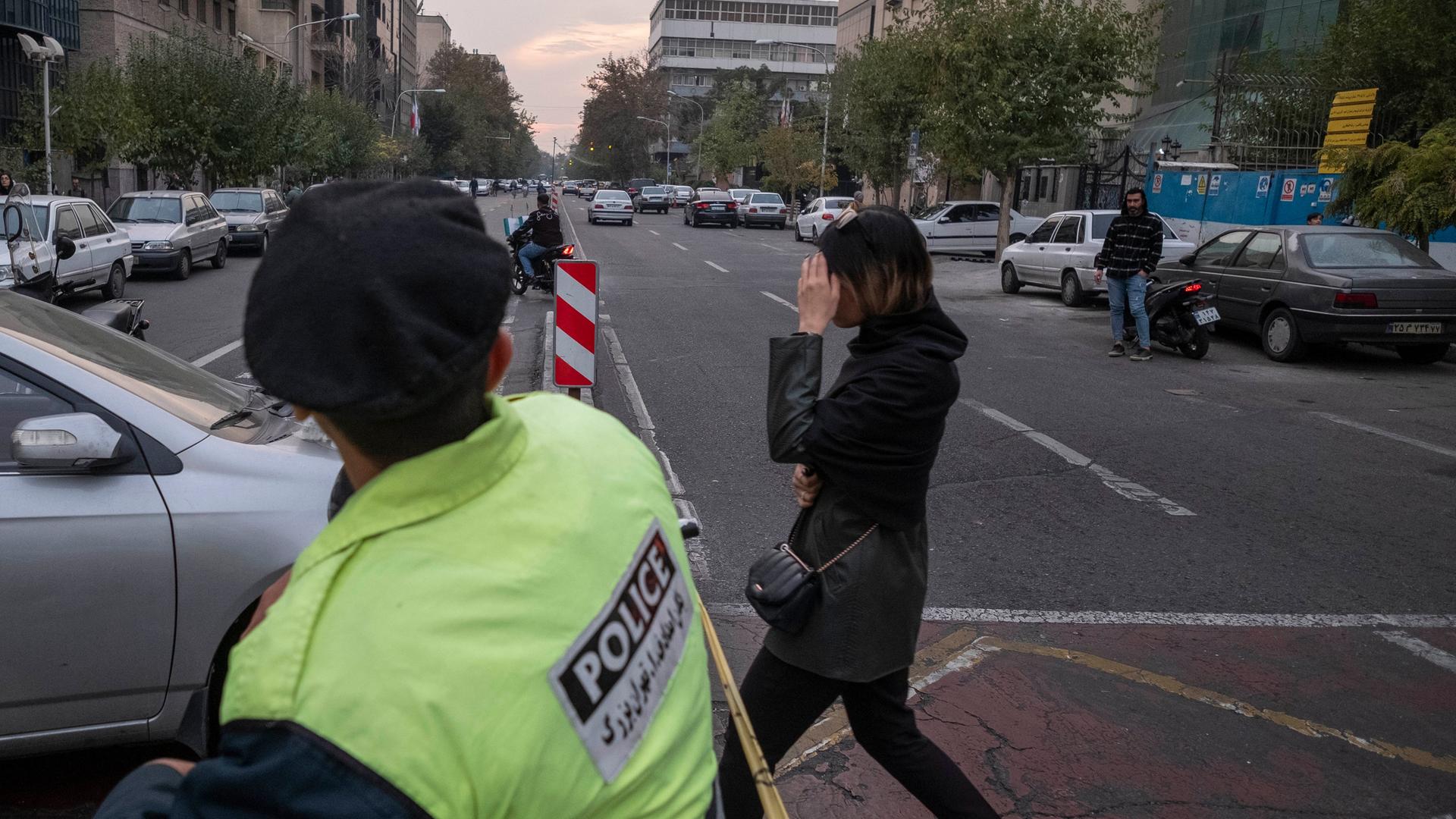 Eine junge Frau überquert in Teheran vor einem Polizisten ohne den verpflichtenden Schleier eine Straße. Sie versucht mit der Hand ihr Gesicht zu verbergen.