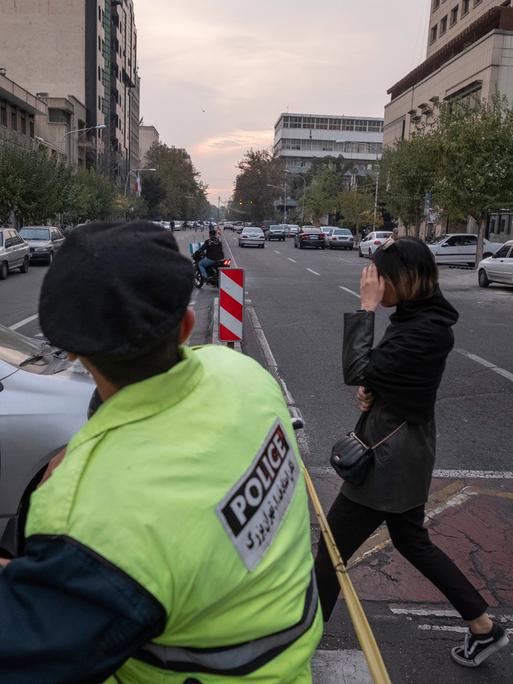 Eine junge Frau überquert in Teheran vor einem Polizisten ohne den verpflichtenden Schleier eine Straße. Sie versucht mit der Hand ihr Gesicht zu verbergen.