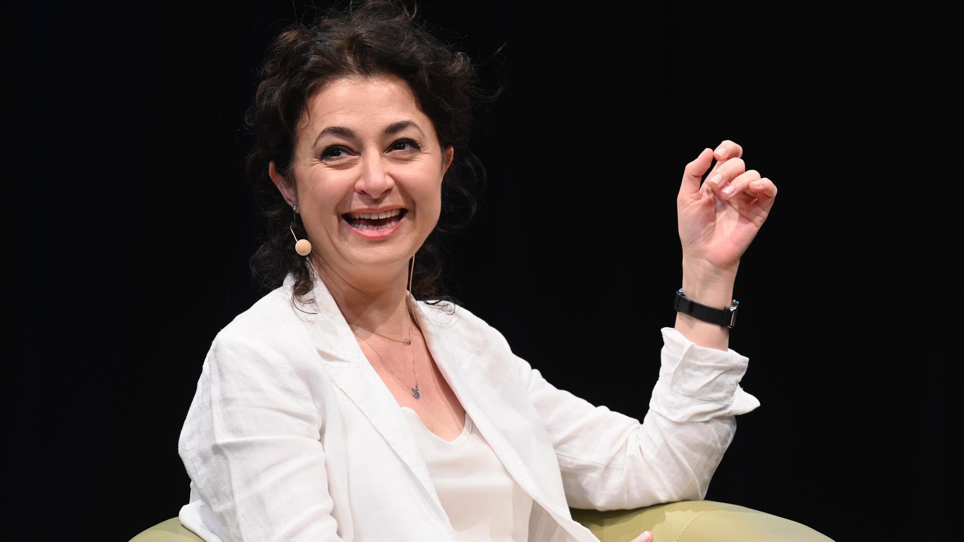 Ece Temelkuran spricht lächelnd auf einem Podium und trägt weiße Kleidung vor dunklem Hintergrund Ece Temelkuran spricht lächelnd auf einem Podium und trägt weiße Kleidung vor dunklem Hintergrund