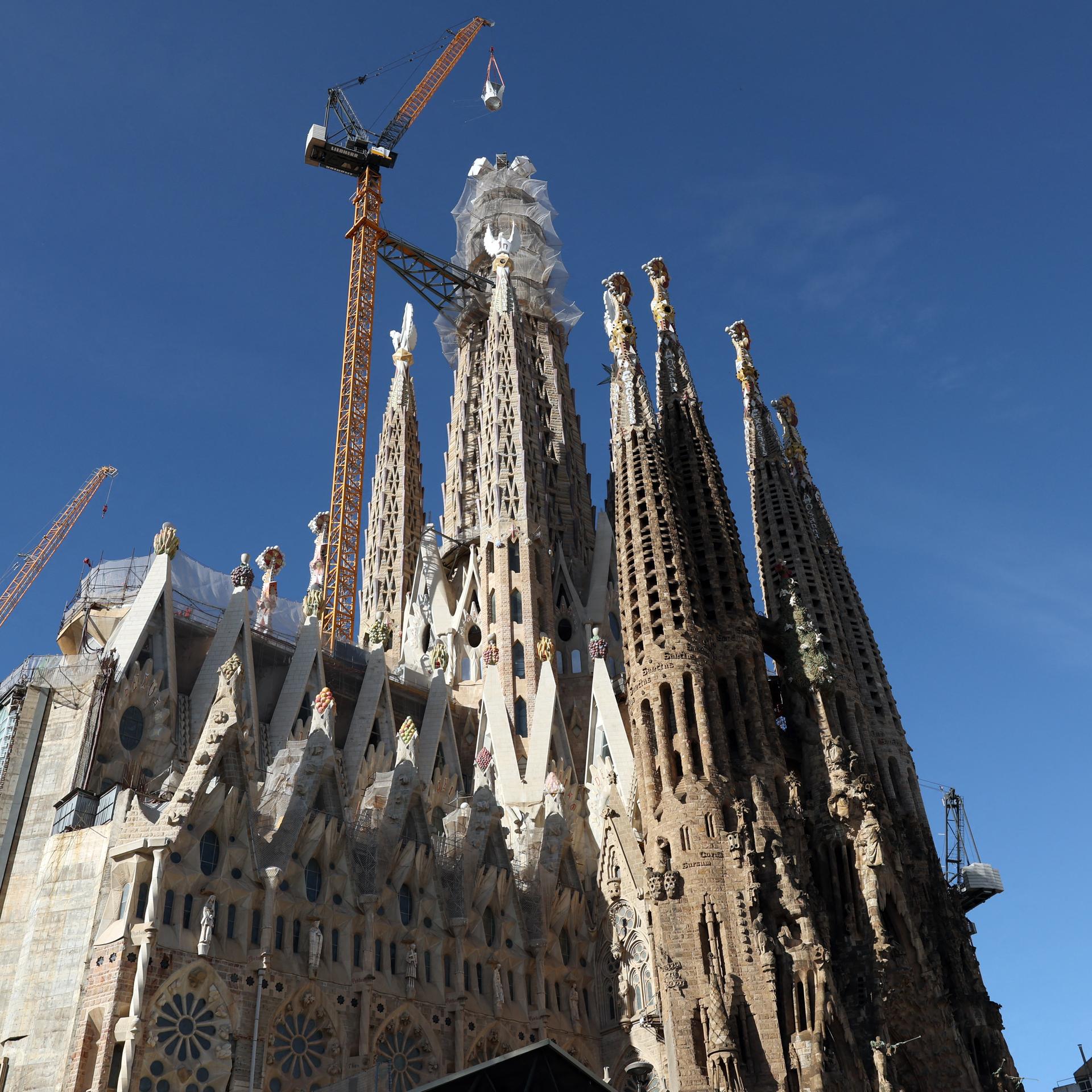 Ein Kran hebt das letzte Teilstück eines Kreuzes auf den Turm der Sagrada Familia in Barcelona.