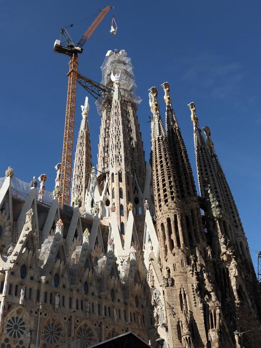 Ein Kran hebt das letzte Teilstück eines Kreuzes auf den Turm der Sagrada Familia in Barcelona.