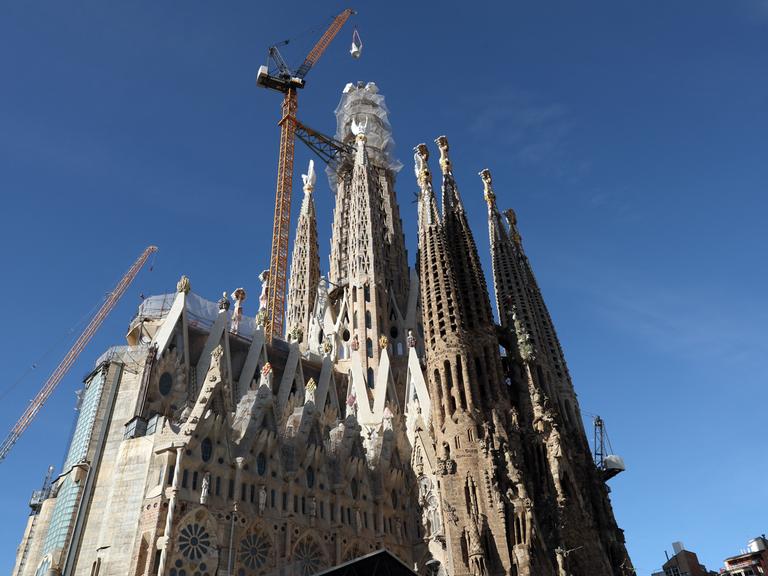 Ein Kran hebt das letzte Teilstück eines Kreuzes auf den Turm der Sagrada Familia in Barcelona.