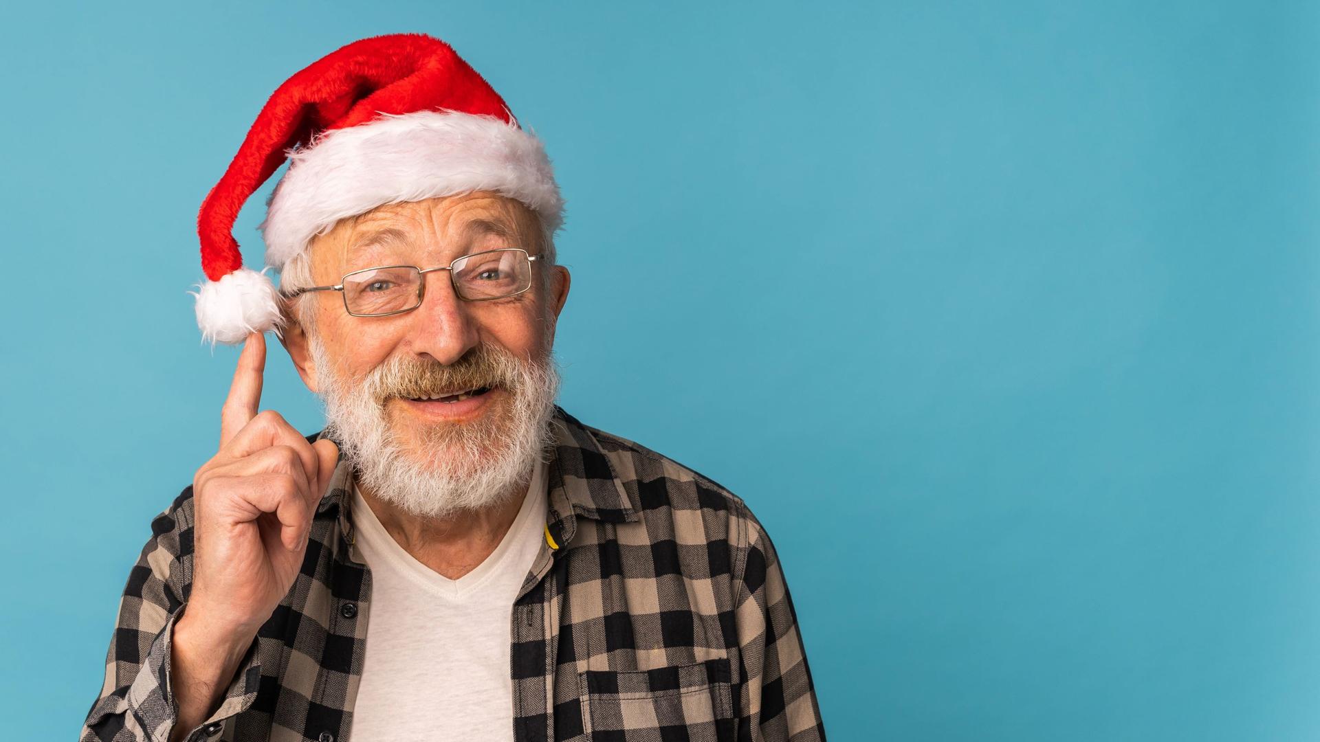 Ein älterer Mann hat eine Nikolausmütze auf dem Kopf und fasst schelmisch an den Bommel seiner Mütze.