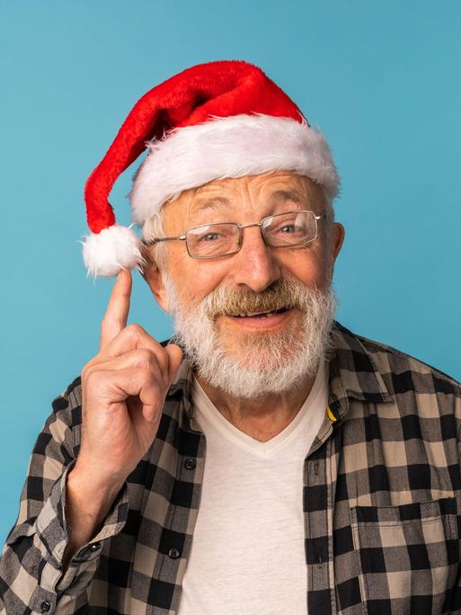 Ein älterer Mann hat eine Nikolausmütze auf dem Kopf und fasst schelmisch an den Bommel seiner Mütze.