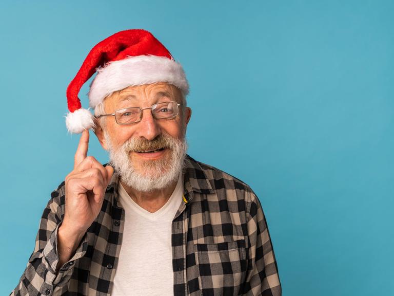 Ein älterer Mann hat eine Nikolausmütze auf dem Kopf und fasst schelmisch an den Bommel seiner Mütze.